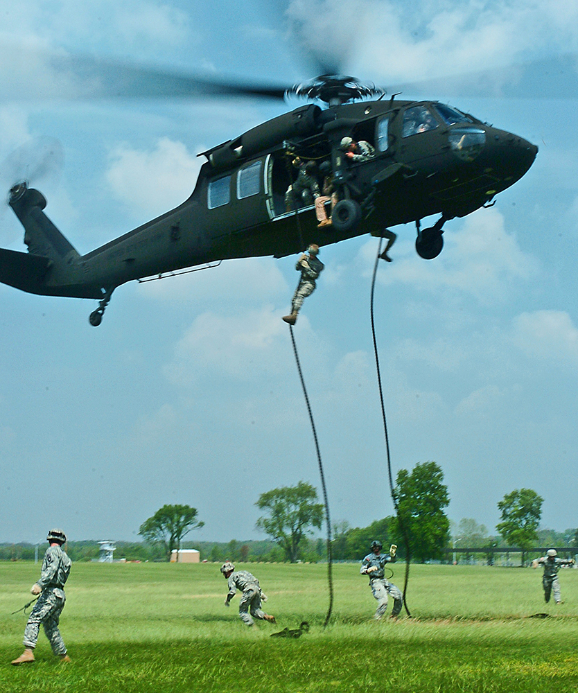 soldiers sliding down rope from hovering helicopter onto grass field